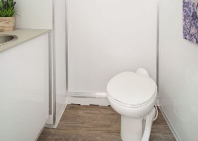 Interior of a luxury portable restroom featuring wood-style flooring, a porcelain flush toilet, and modern white cabinetry for a high-end feel.