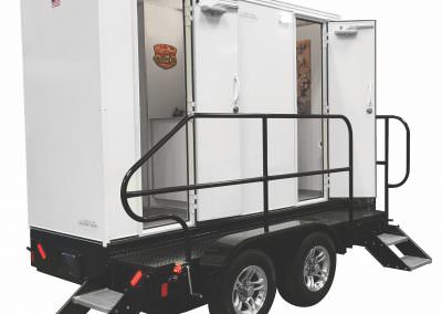 High-capacity luxury event restroom trailer featuring separate men’s and women’s entrances with sturdy handrails and chrome-accented wheels.